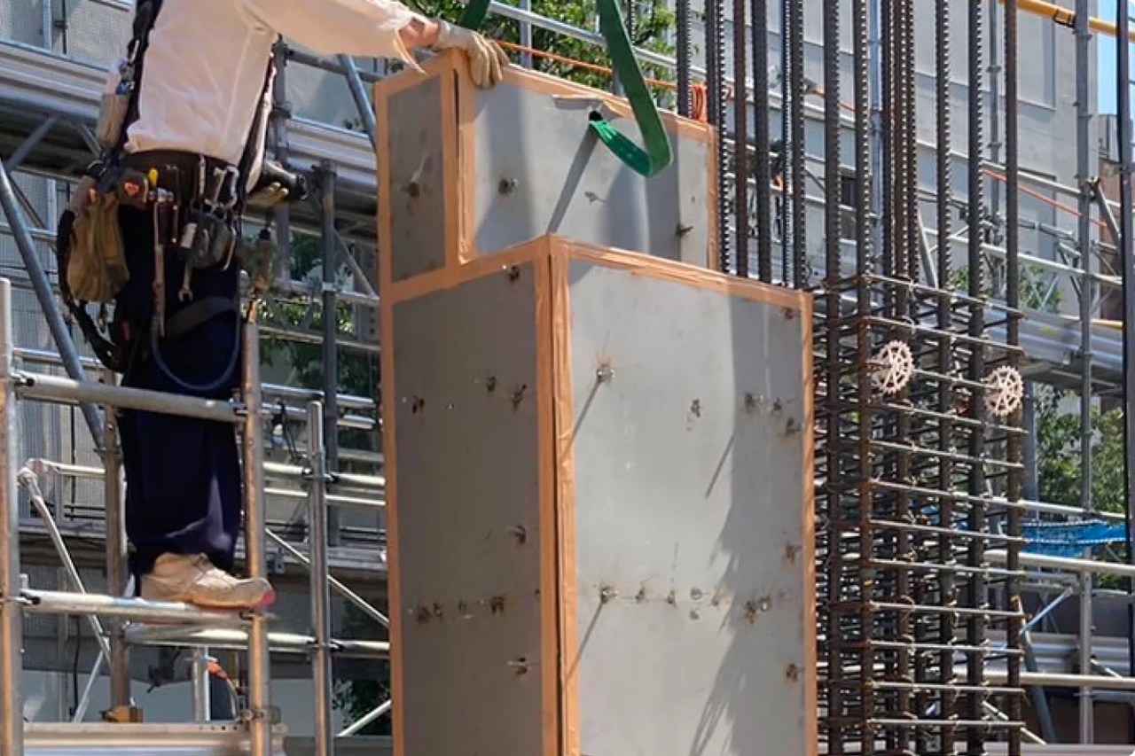 建設現場：作業員が高所足場で鉄骨構造物に型枠を吊り上げている様子。