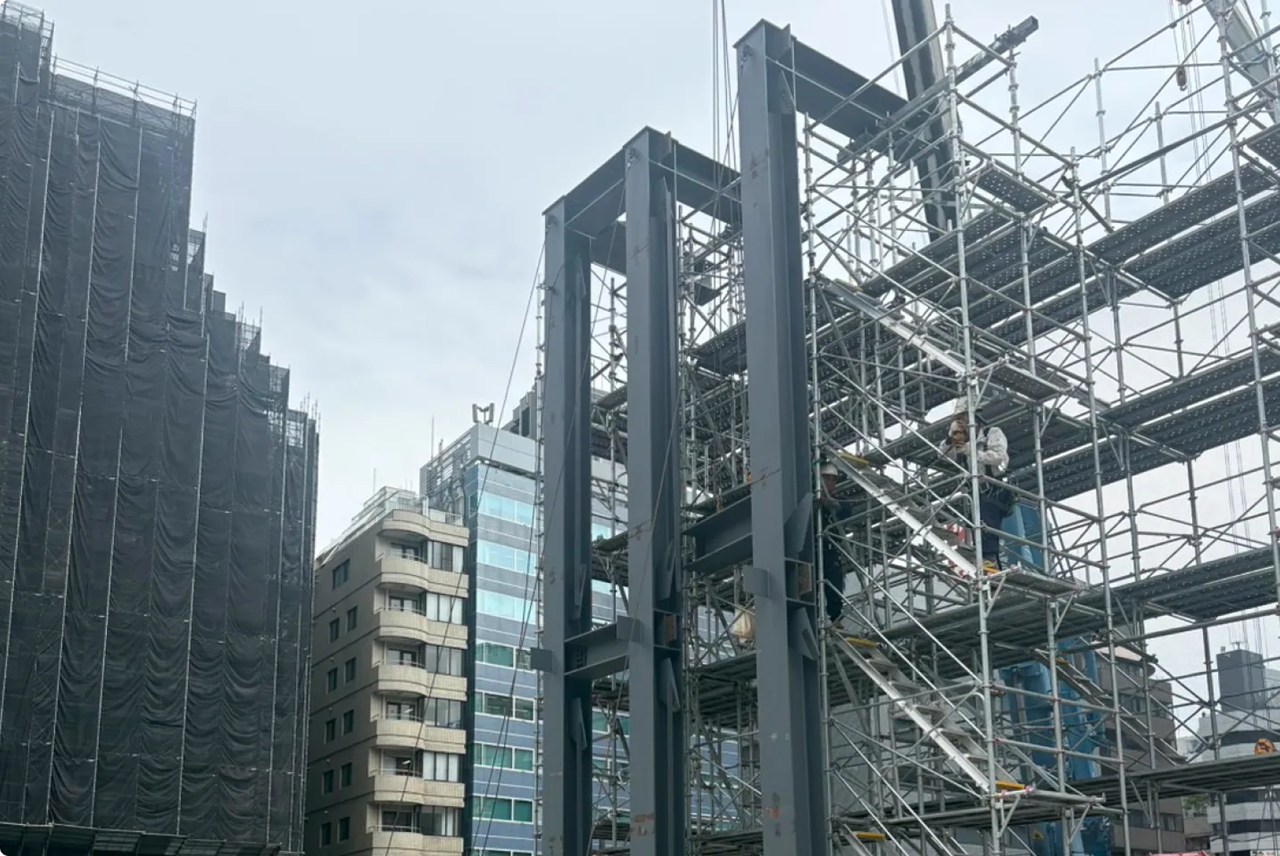 巨大なグレーの鉄骨がそびえ立つ建設現場の様子。